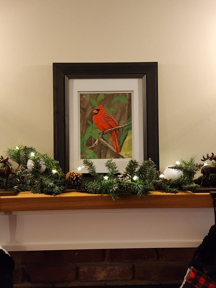 Framed artwork of a cardinal bird on a wall with Christmas decorations.